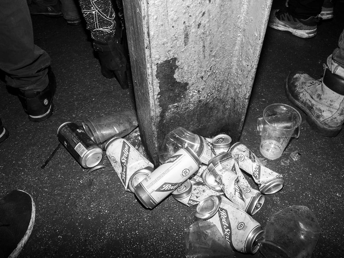 A pile of crushed beer cans on the floor by a pillar. The muddied feet of dancers in the background.